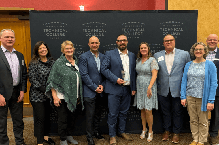 Group of nine individuals posing with an award in front of a Wisconsin Technical College System banner.