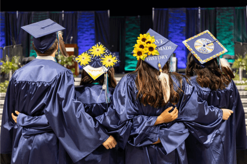 Graduates linked arms with their graduation caps displayed