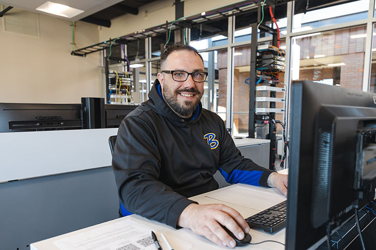 IT student works on computer with hardware in background