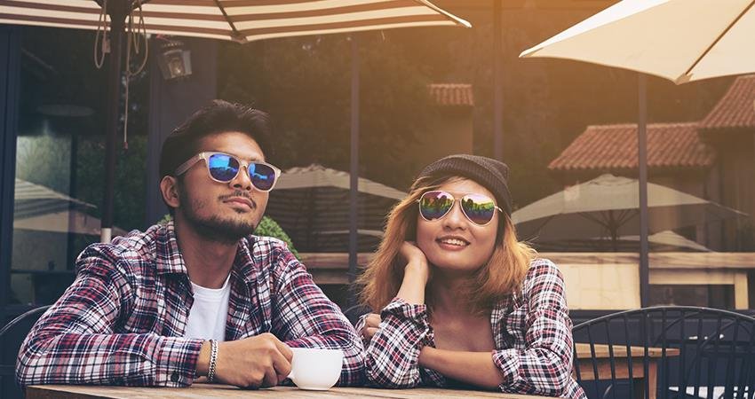 Two Students wearing sunglasses and drinking coffee on an outside patio.