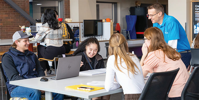 Advisor laughs with students sitting around a table
