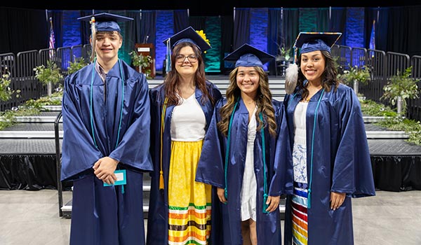 Four graduates in cap and gowns posing together