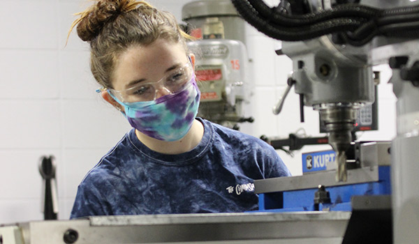 Female student wears a mask and works on a cnc machine tool 