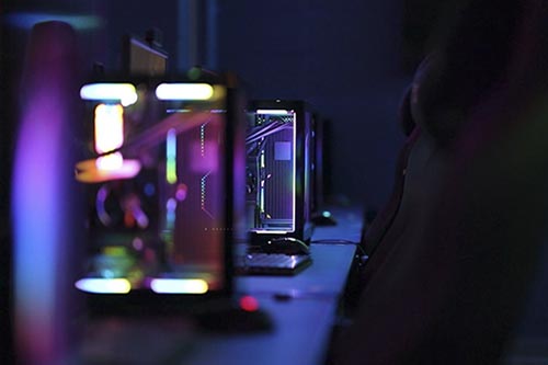 Computer desks and chairs in front of glowing computers, keyboards, and mice