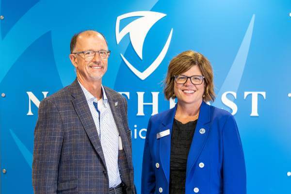Dan Verbanac and Kristen Raney stand in front of wall with NWTC logo; both are smiling at camera