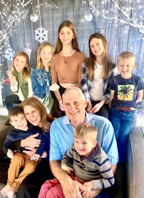 Mary Beth Boettcher sitting with husband and seven grandchildren