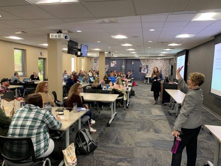 Room full of people watching a presentation.