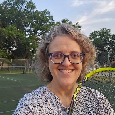 Jennifer Flatt, facing camera, smiling and holding tennis racket