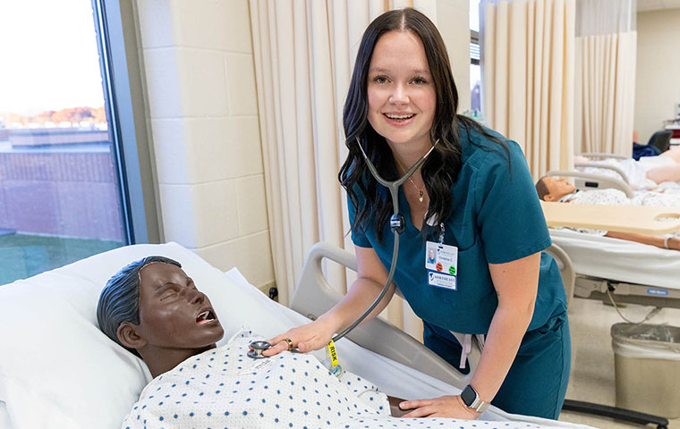 Nursing student smiles whlie checking on a sim patient
