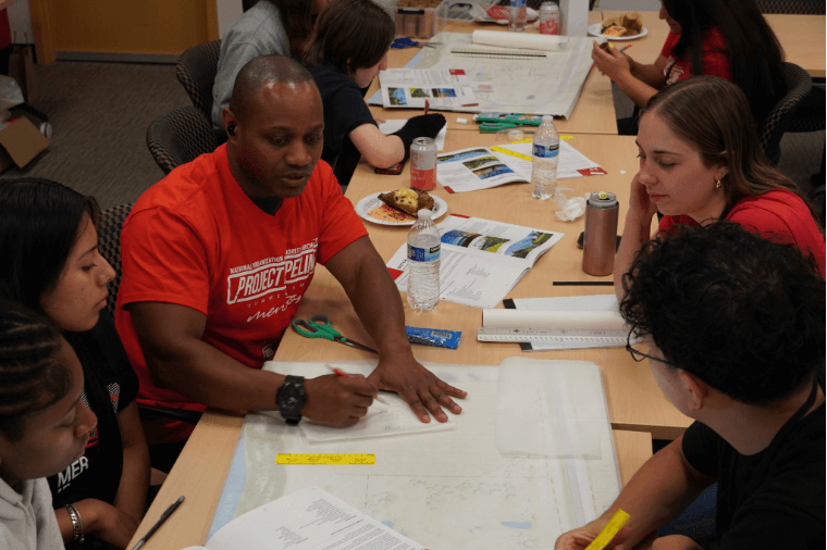 Group of people collaborating over a map at a table, with one wearing a "Project Pipeline" t-shirt.