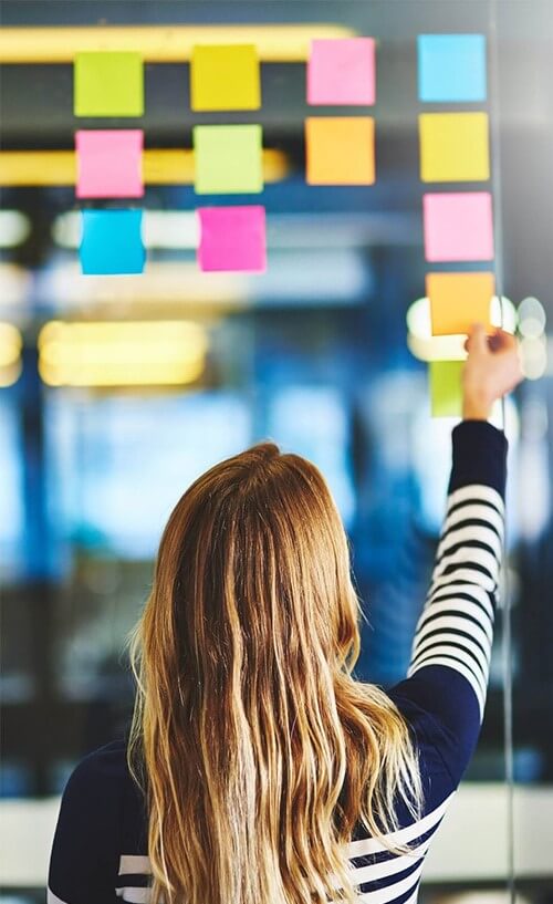 Person placing colorful sticky notes on a glass wall during a planning or brainstorming session.