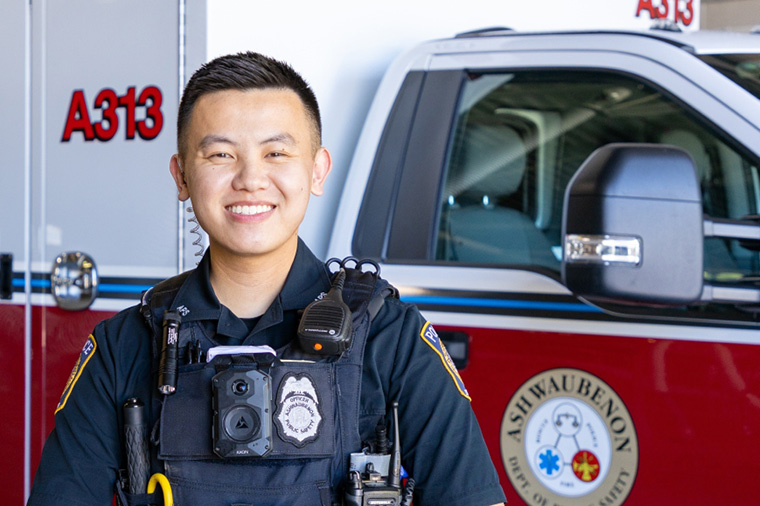 Smiling EMT student stands in front of ambulance