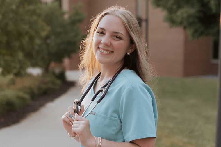 Smiling nursing student holds stethoscope outside building
