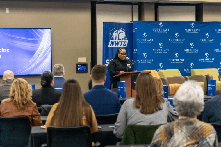 Cora Jenkins stands in front of a podium giving her speech to attendees at NWTC's annual State of the College.